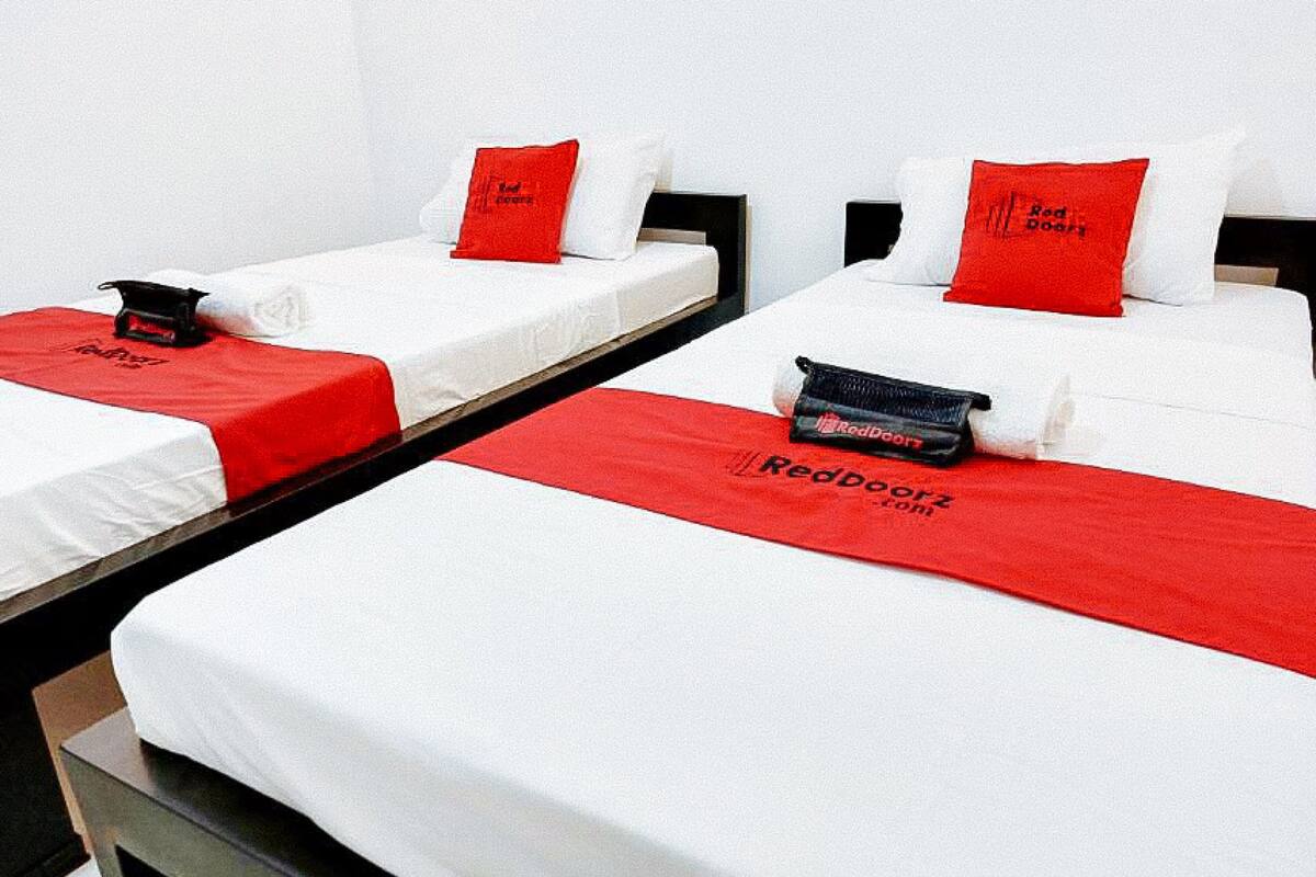 A hotel room with three single beds, each with a white mattress and red bedding.