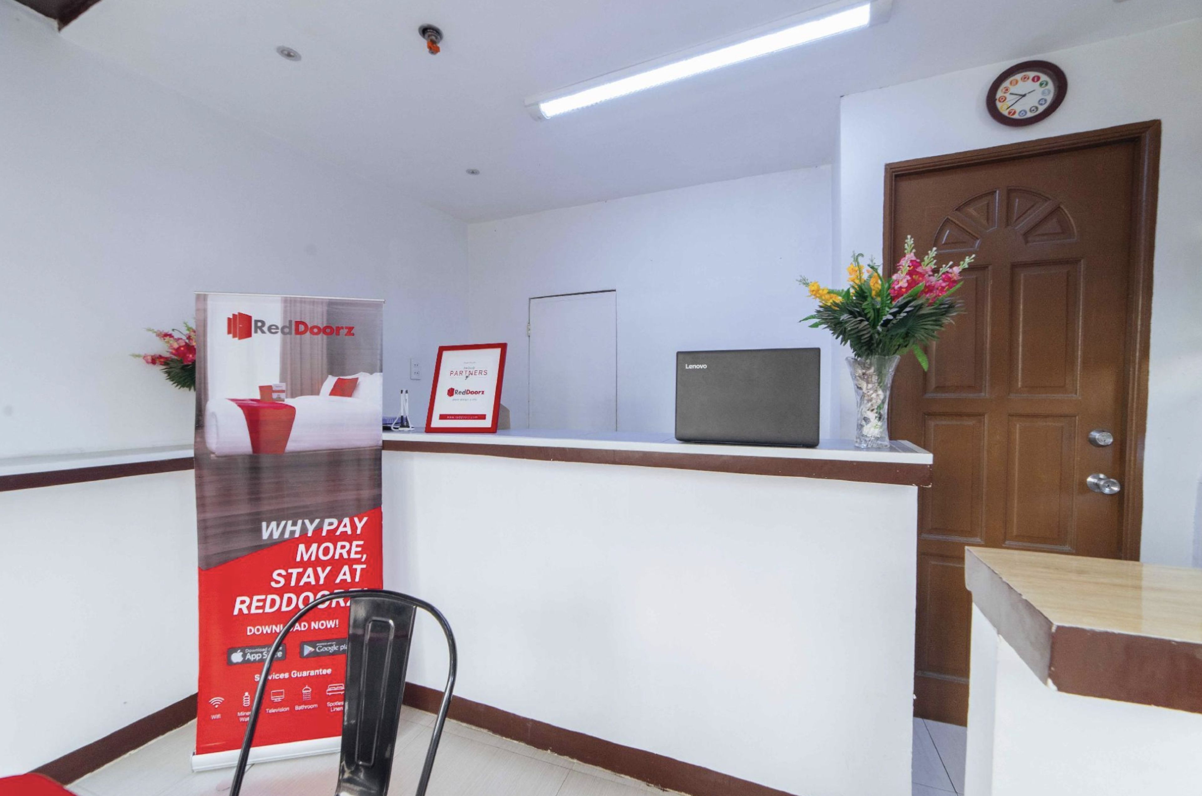 A reception area with a RedDoorz advertisement, a television, a wooden door, and a clock on the wall.
