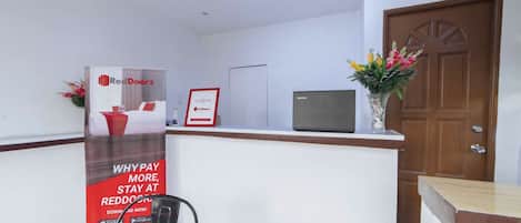 A reception area with a RedDoorz advertisement, a television, a wooden door, and a clock on the wall.