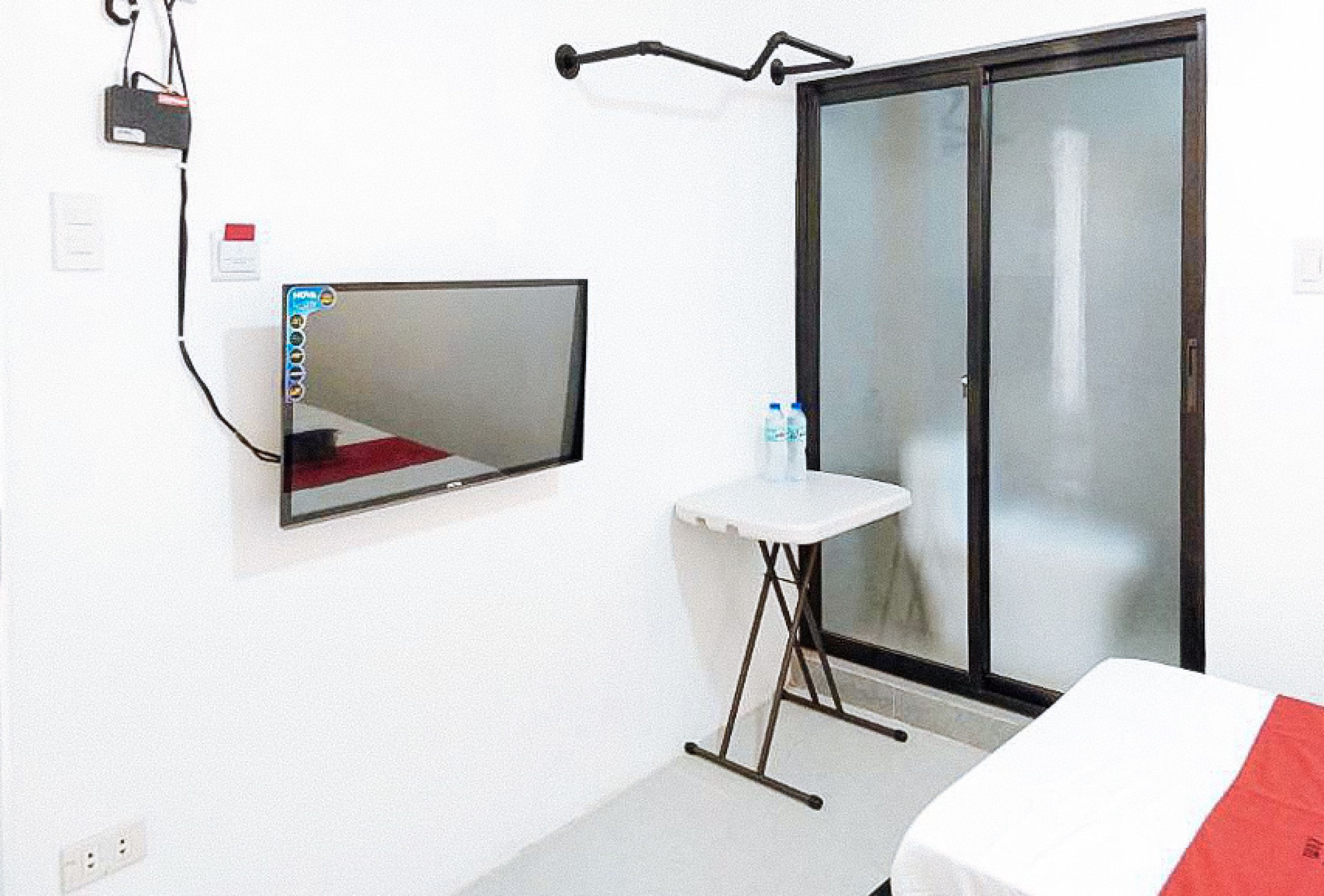 Une chambre d’hôtel comprenant un lit, une petite table avec une chaise, un miroir, une porte-fenêtre coulissante et une prise de courant.