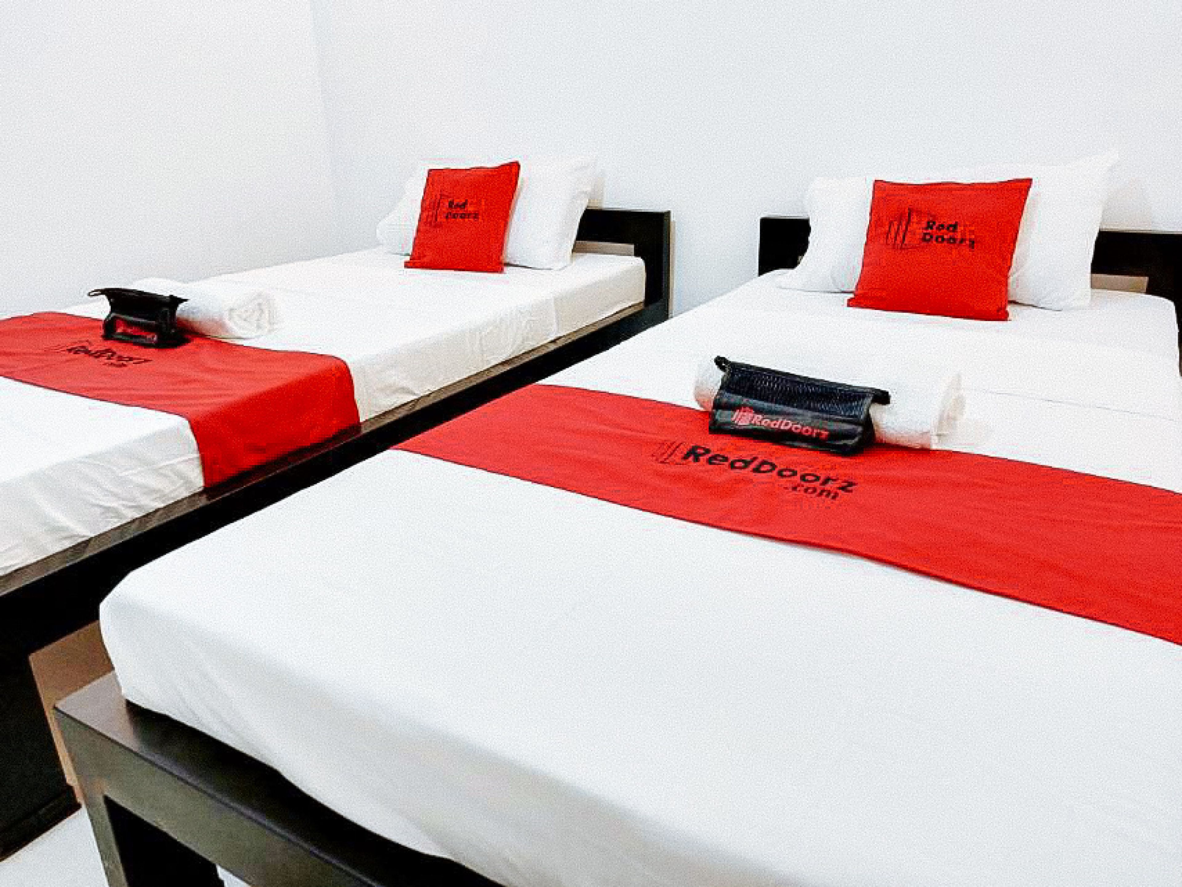 A hotel room with three single beds, each with a white mattress and red bedding.
