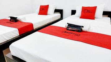 A hotel room with three single beds, each with a white mattress and red bedding.