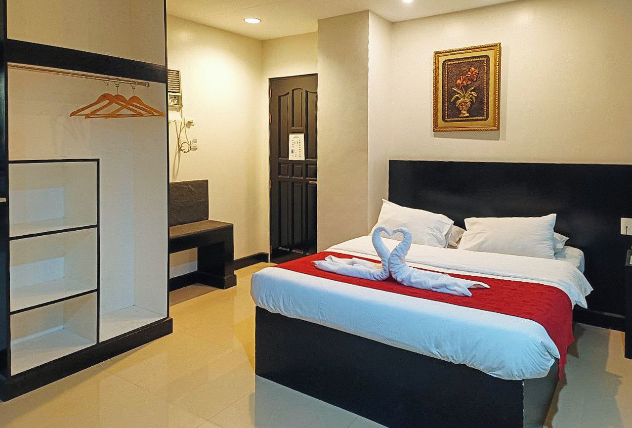 A hotel room with a bed, a wardrobe, a desk, and a wall-mounted picture.