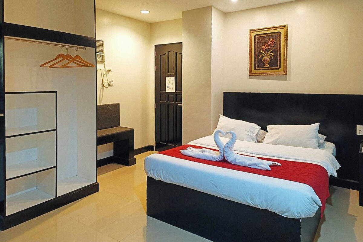 A hotel room with a bed, a wardrobe, a desk, and a wall-mounted picture.
