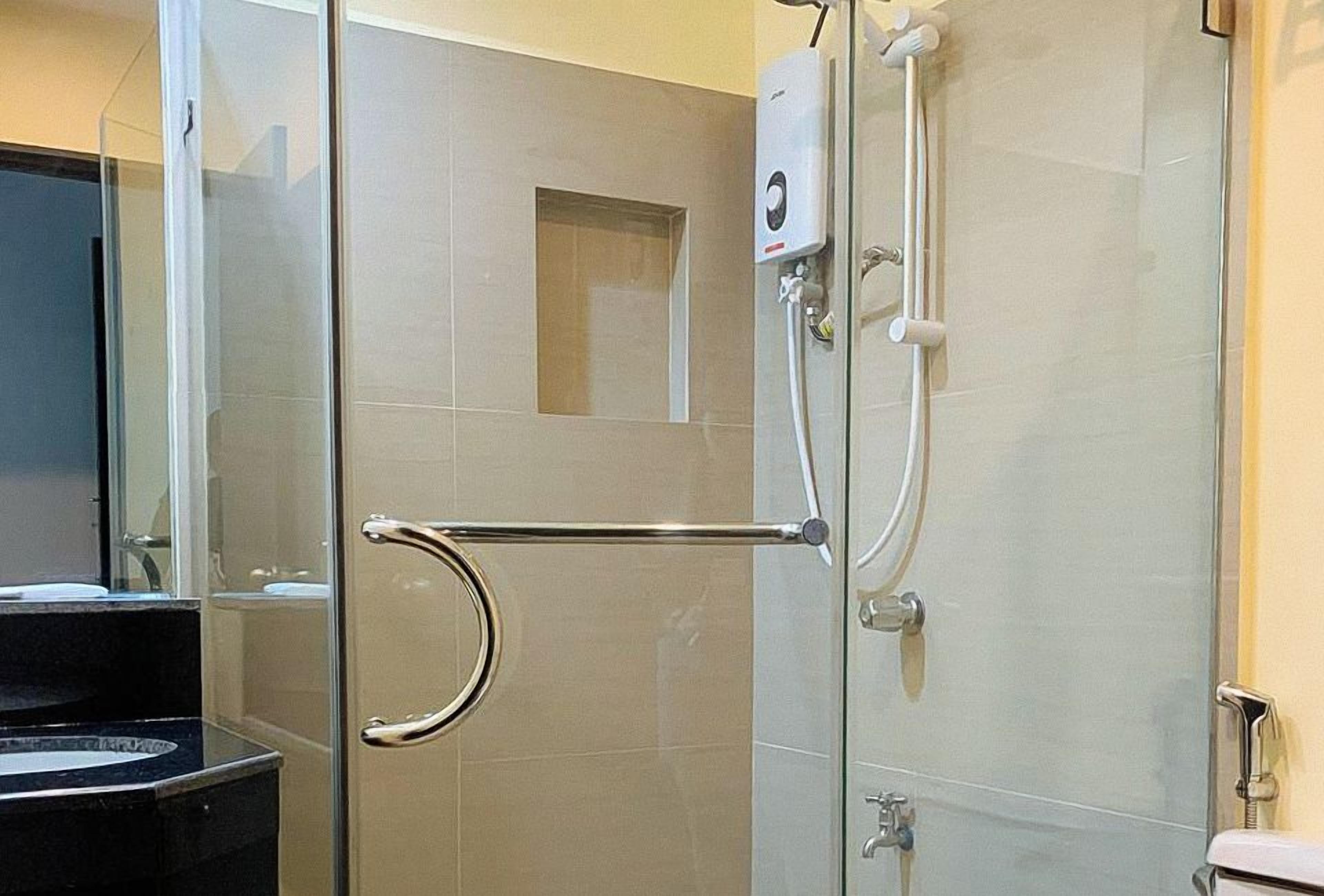 A modern bathroom with a glass shower enclosure, a handrail, a toilet, and a sink.