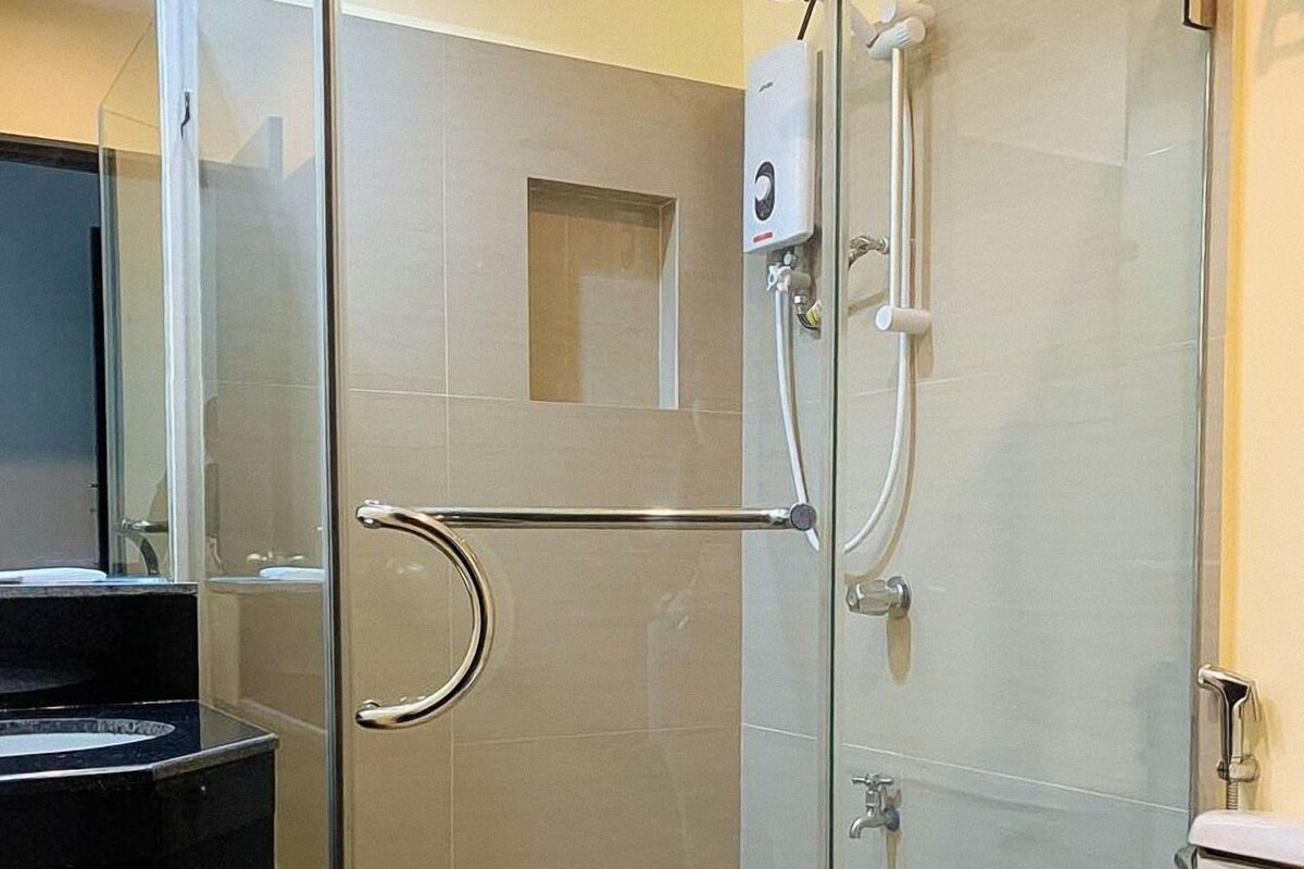 A modern bathroom with a glass shower enclosure, a handrail, a toilet, and a sink.