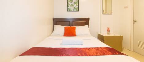 A neatly made bed with white and red bedding, a wooden headboard, a small bedside table with a vase of flowers, and a framed picture on the wall.