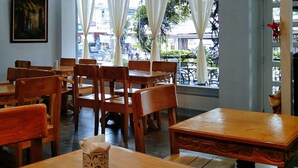 A restaurant interior with wooden tables and chairs, a painting on the wall, and a view of the street outside. - Check Inn Hotel Dumaguete City By Reddoorz (Dumaguete)