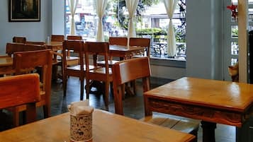 A restaurant interior with wooden tables and chairs, a painting on the wall, and a view of the street outside.
