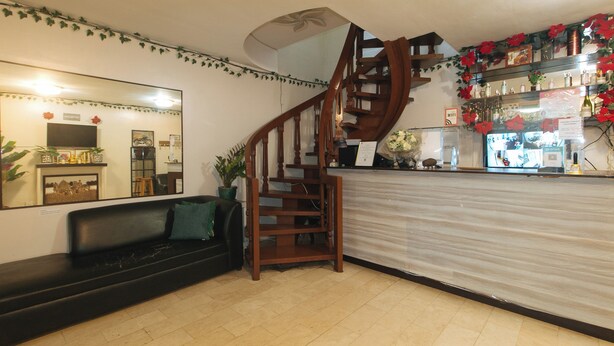 A staircase leading to a second floor, a reception desk with a mirror, a black leather sofa, and a potted plant. - Check Inn Hotel Dumaguete City By Reddoorz (Dumaguete)