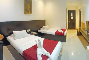A hotel room with two beds, each with white and red bedding, a small bedside table with a lamp, and a framed picture on the wall. - Check Inn Hotel Dumaguete City By Reddoorz (Dumaguete)
