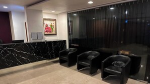 Una zona de recepción con mostrador de mármol, tres sillas negras y un cuadro en la pared.