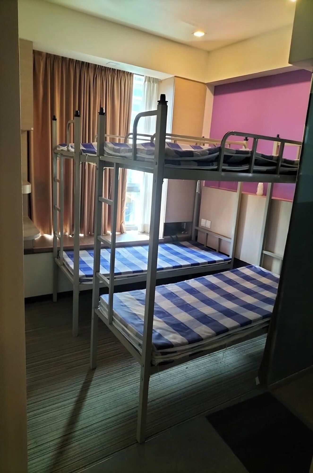 Een slaapkamer met stapelbed, raam, gordijnen en een roze muur.