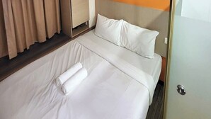 Habitación de hotel con cama, cortinas, armario y una pared de acento naranja.