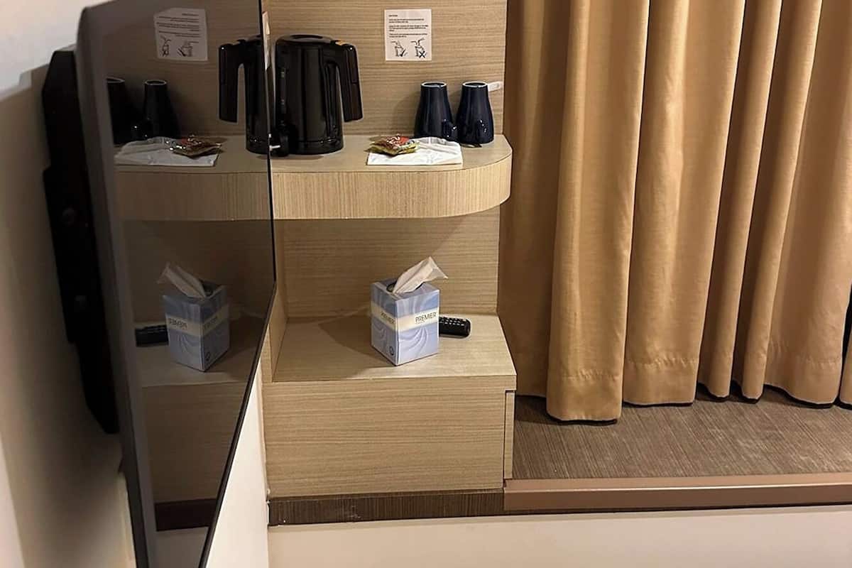 Une chambre d’hôtel avec un lit, un téléviseur fixé au mur, une petite table avec une machine à café, des tasses et des mouchoirs.