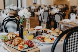 A dining table set with a variety of breakfast items including croissants, fruits, and pastries, with a vase of flowers and glasses of orange juice and champagne. - Miramare (Crikvenica)
