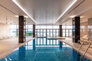 An indoor swimming pool with clear views of the sea, surrounded by lounge chairs and a modern interior design. - Miramare (Crikvenica)