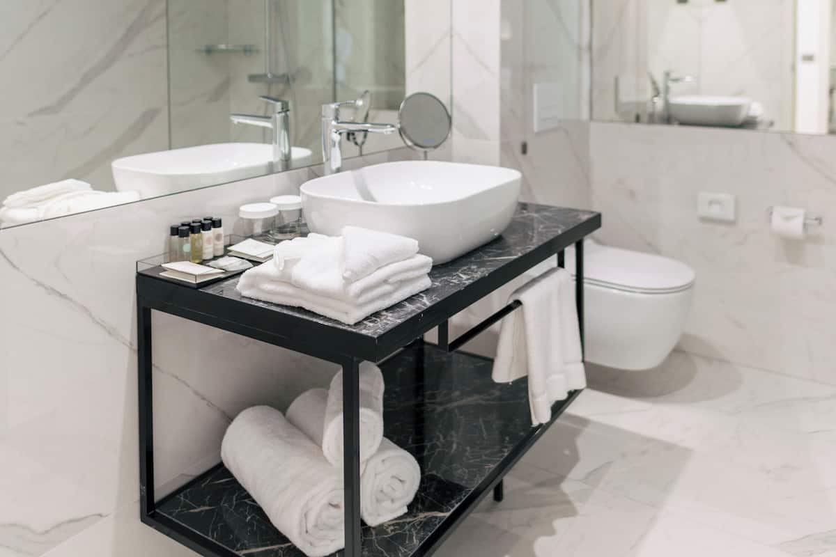 A modern bathroom with a large mirror, two sinks, a black vanity, and a toilet.
