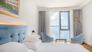 A hotel room with a large bed, two armchairs, a small table, a lamp, and a window with a view of the water. - Miramare (Crikvenica)