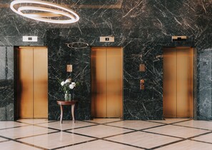 A modern elevator area with marble walls, a wooden floor, and a vase of white flowers. - Miramare (Crikvenica)