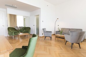 Un salon moderne avec un parquet en bois disposé en motif «point de Hongrie», un fauteuil vert, un fauteuil gris, un canapé gris et une petite table.