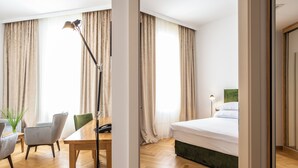 A hotel room with a wooden floor, a bed with a green headboard, a desk with a telephone, and a chair. - Miramare (Crikvenica)