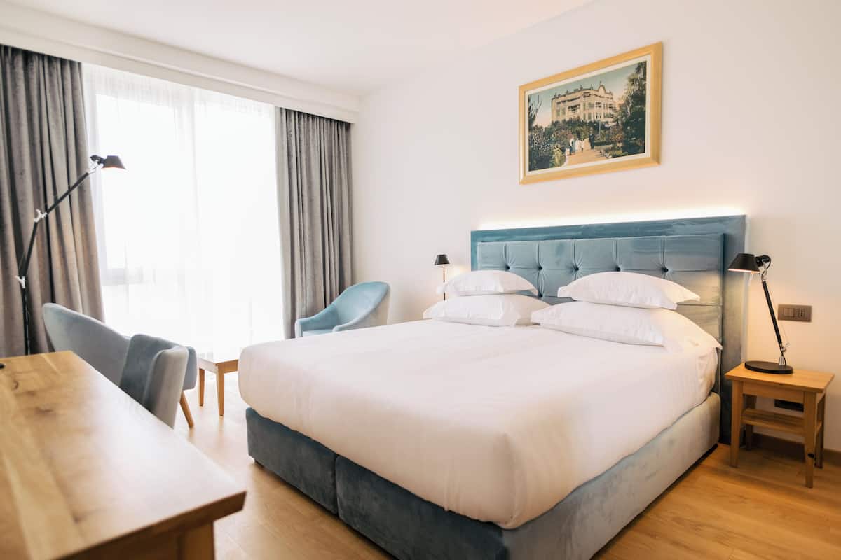 A hotel room with a large bed, a desk, a chair, and a small table.