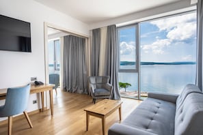 A modern living room with a sofa, a coffee table, a desk with a chair, a television, and a large window with a view of the sea. - Miramare (Crikvenica)