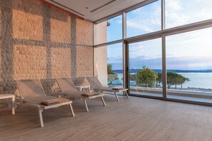 A spa area with three sun loungers, a stone wall, and a large window offering a view of the sea. - Miramare (Crikvenica)