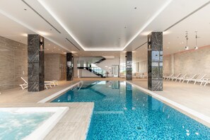 An indoor swimming pool with clear water, surrounded by lounge chairs and a modern interior design. - Miramare (Crikvenica)
