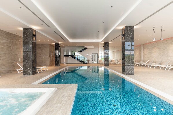Une piscine intérieure à l’eau claire, entourée de chaises longues et dotée d’un aménagement intérieur moderne.