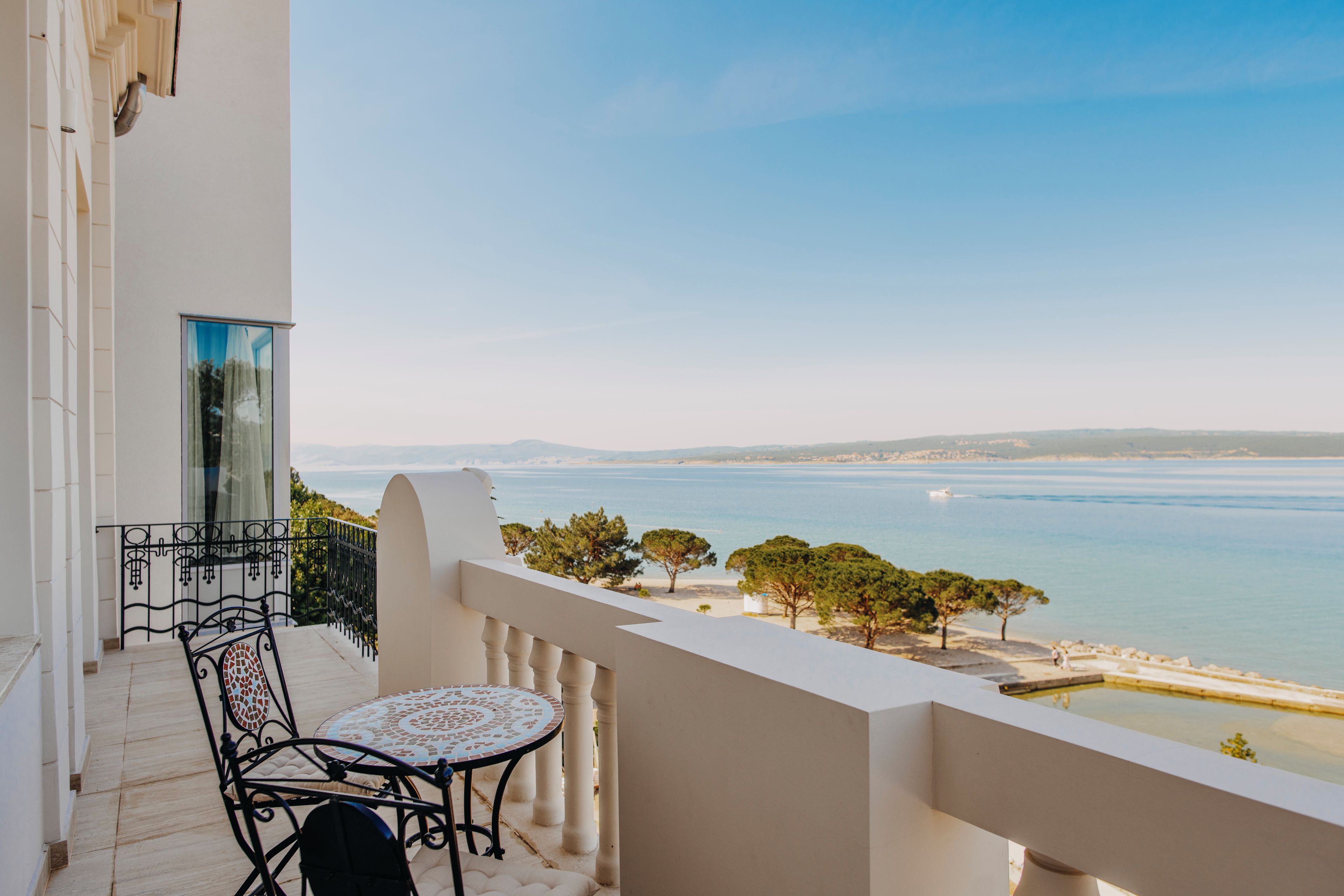 A balcony with a table and chairs overlooking a coastal view.