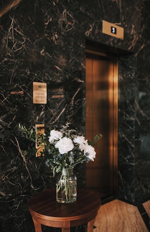 A marble wall with a wooden table holding a vase of flowers, an elevator, and a sign with the number 5. - Miramare (Crikvenica)