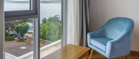 A room with a large window, a blue armchair, and a wooden table.