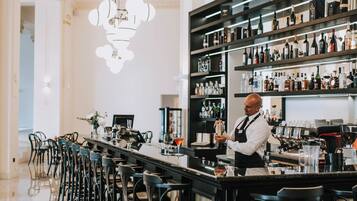 Un'area bar con un barista, un lungo bancone e diversi sgabelli.