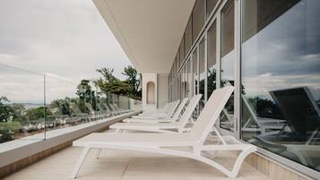 A modern outdoor lounge area with white lounge chairs and a glass balustrade overlooking a scenic landscape.