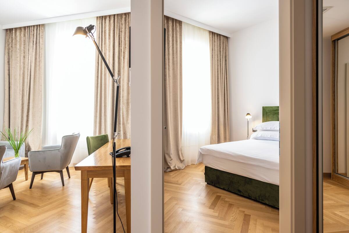 Hotellihuone, jossa on puulattia, vihreäpäätyinen sänky, työpöytä, jossa on puhelin, ja tuoli.