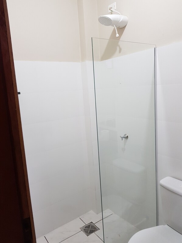 A glass-enclosed shower stall with a white ceiling-mounted showerhead. - Hotel Itatiaia (Tangará da Serra)