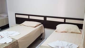 A hotel room with two beds, each with a headboard and a pillow. There is a small table with a towel and a bottle on it.