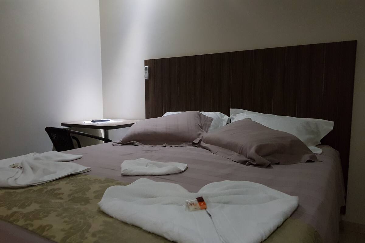 A neatly made bed with pillows and a folded towel on a patterned bedspread.