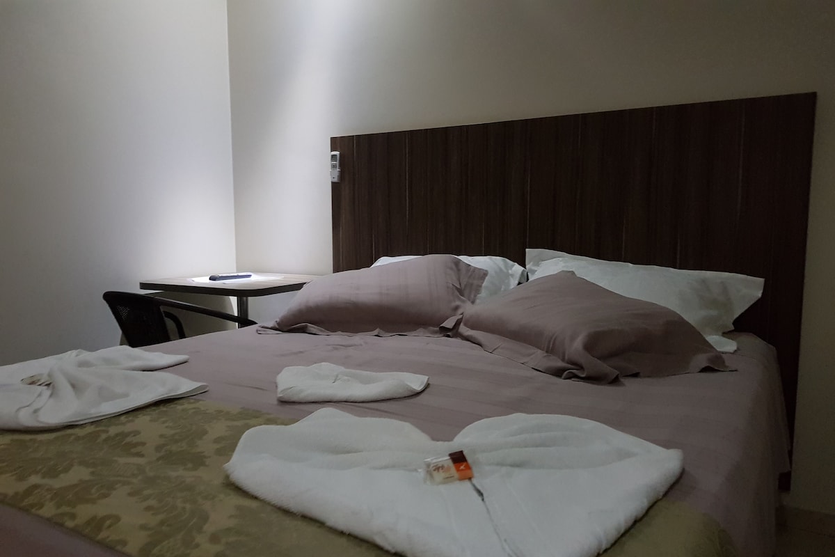 A neatly made bed with pillows and a folded towel on a patterned bedspread.
