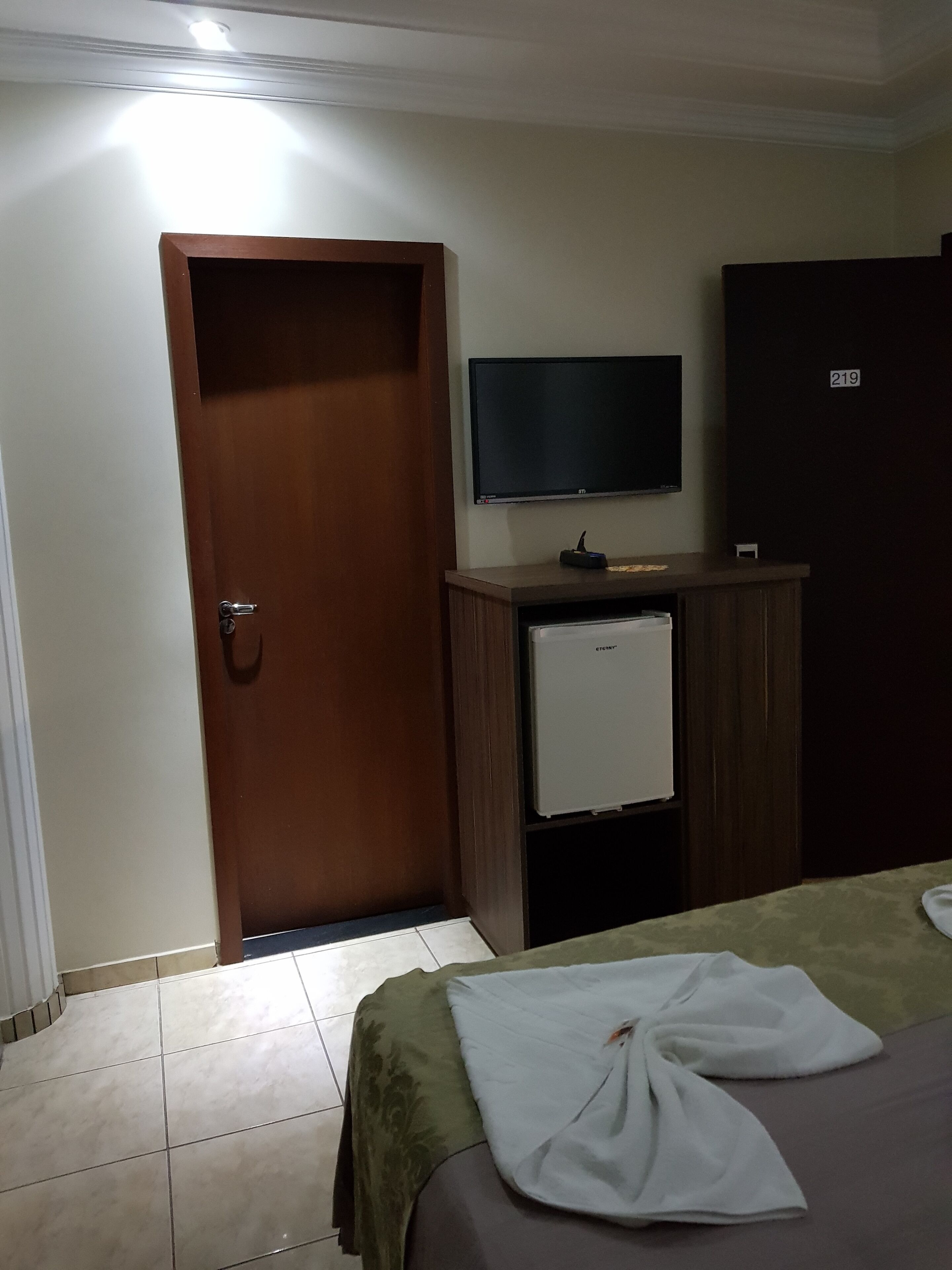 Una habitación de hotel con cama, televisión, minibar y puerta.