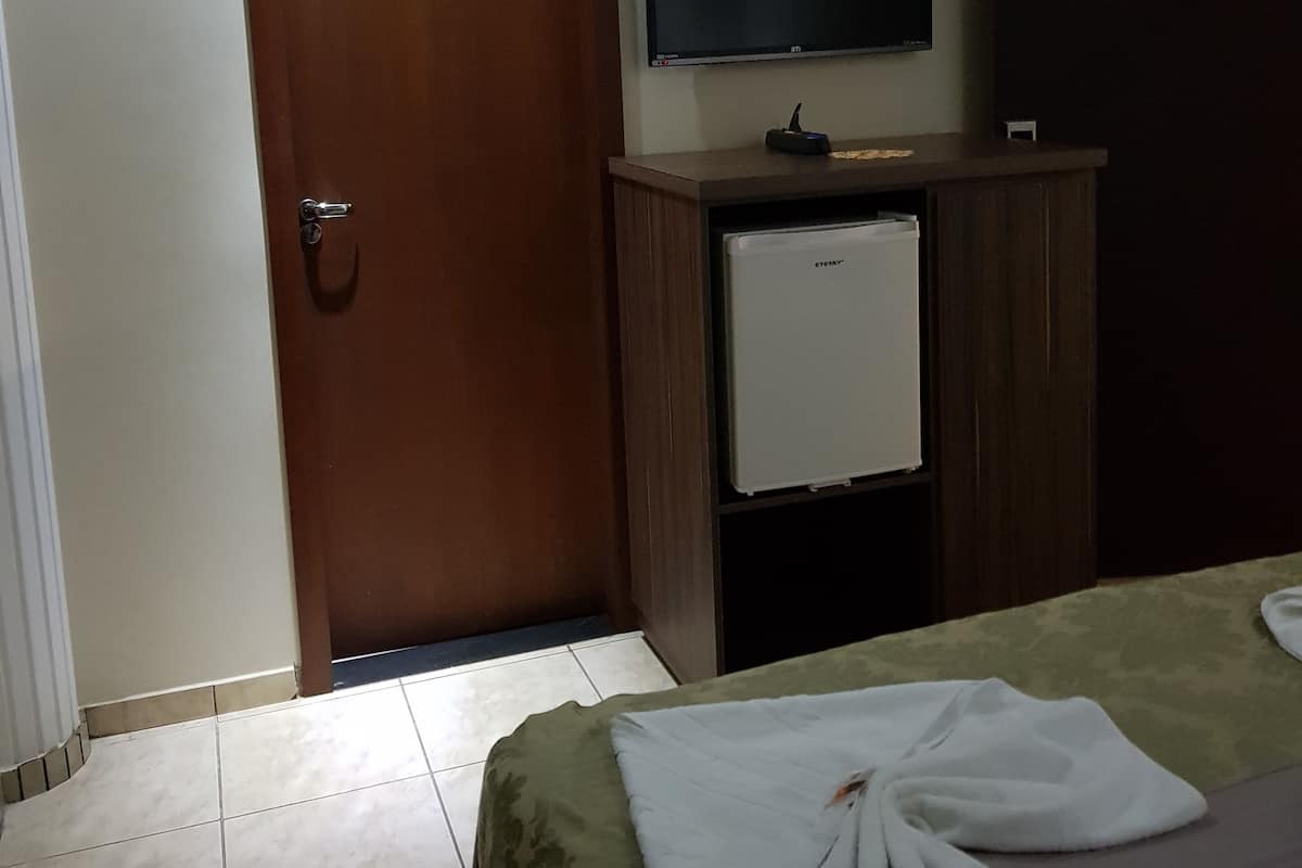 A hotel room with a bed, a television, a minibar, and a door.