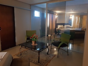 A hotel room with a glass partition, a dining table with chairs, a small potted plant, and a bed with a white comforter. - Hotel Itatiaia (Tangará da Serra)