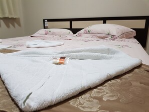 Un lit bien fait, recouvert d’une couvre-lit à motifs floraux, avec une serviette blanche et un flacon de lotion posés sur le lit.