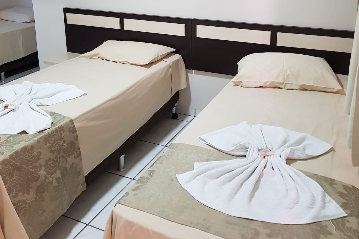A hotel room with two beds, each with a headboard and a pillow. There is a small table with a towel and a bottle on it.