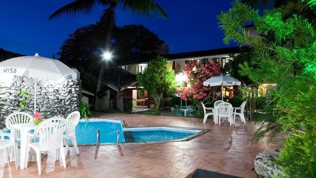 A pool area with white chairs and tables, a stone wall, and a Visa-branded umbrella. - Chaua Porto Hotel (Porto Seguro)