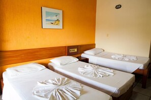 Une chambre d’hôtel avec trois lits simples, chacun agrémenté d’une serviette soigneusement pliée. Un tableau représentant une scène de plage est accroché au mur, au-dessus des lits.