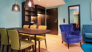 Un espace repas moderne avec une table ronde et des chaises jaunes, un fauteuil bleu et un meuble noir doté d’une porte en verre.