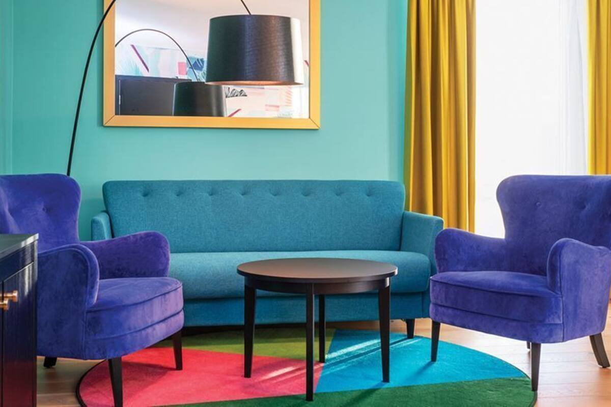 A room with a teal sofa, two blue armchairs, a small round table, and a red and green rug.
